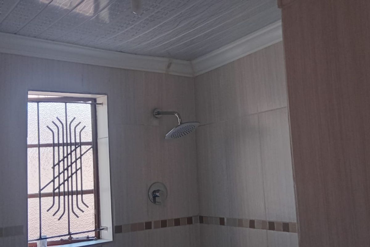 A functional bathroom shower area featuring tiled walls, a modern shower head, and security bars on the window.