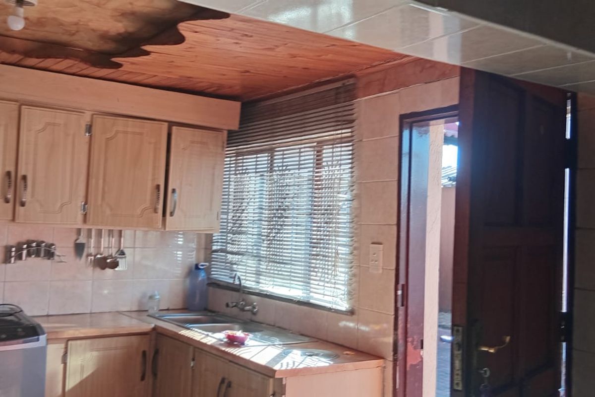 A dated kitchen featuring wooden cabinetry, laminate countertops, a double bowl stainless steel sink, and a timber ceiling with tiled splashback.