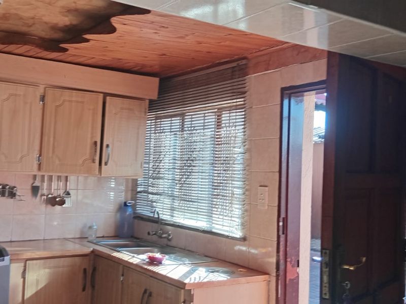 A dated kitchen featuring wooden cabinetry, laminate countertops, a double bowl stainless steel sink, and a timber ceiling with tiled splashback.