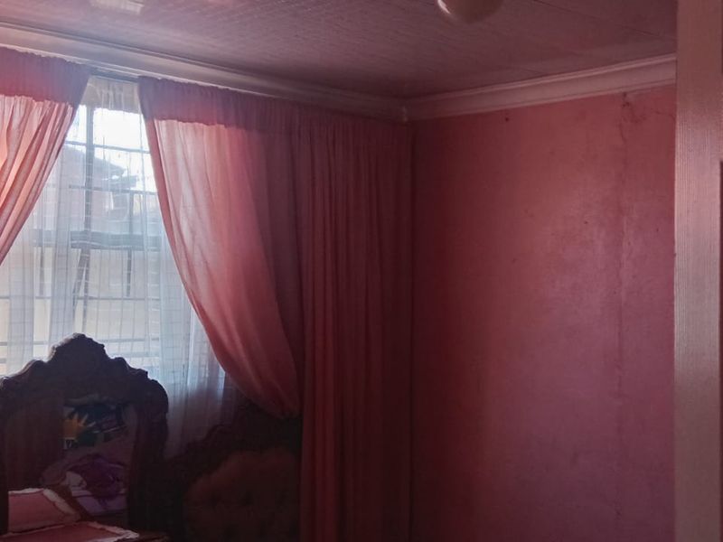 A bedroom featuring pink walls with visible plaster cracking and window security bars, requiring cosmetic updates to improve the overall finish.