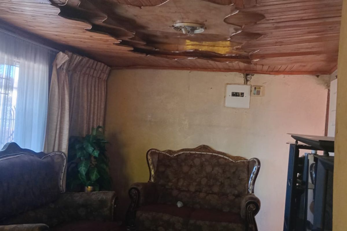 A living room featuring a timber tongue and groove ceiling and an electrical distribution board, currently requiring wall repairs and cosmetic updates.