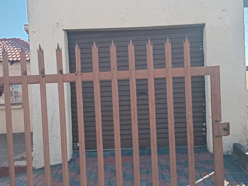 A detached garage featuring a brown roller shutter door, secured by metal fencing and situated on a paved driveway.