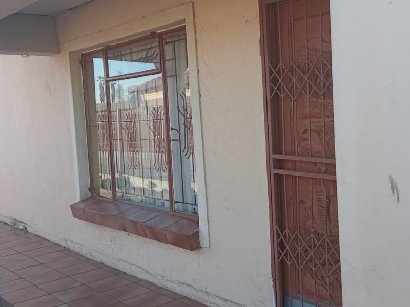 Front entrance area featuring a tiled porch, security gate, and decorative window bars on a single-story residential property.