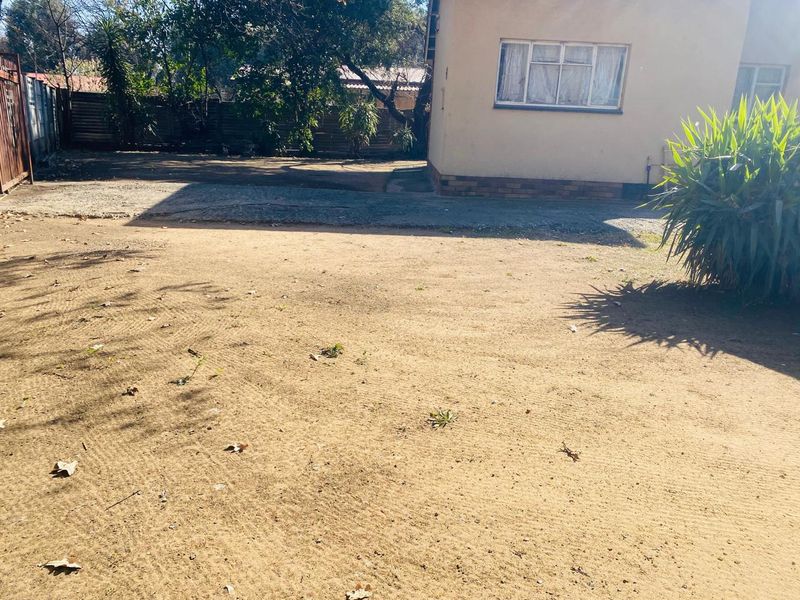 A view of the rear yard area featuring a concrete driveway, perimeter fencing, and the rear elevation of the house with metal window frames.