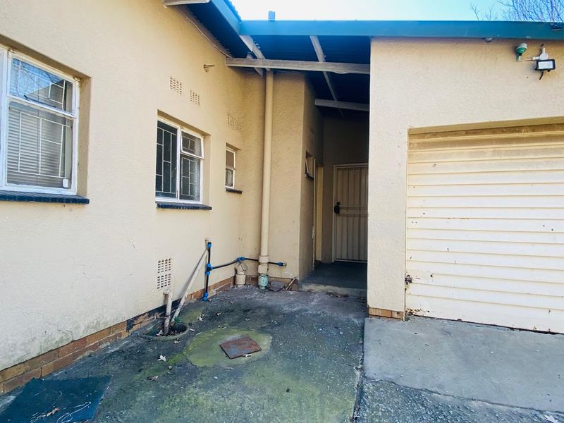 Rear exterior view showing a concrete courtyard area, garage access, and security-fitted windows and doors.
