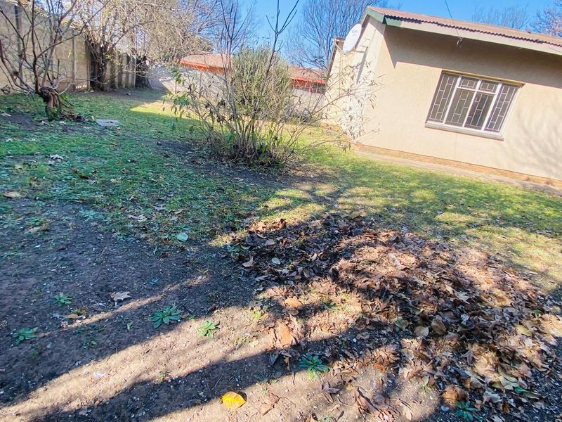 Rear garden area featuring a lawn, perimeter wall, and exterior wall of the house with security bars on the window.