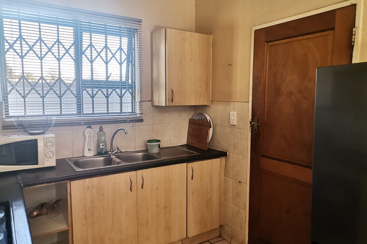 A compact kitchen featuring laminate cabinetry, a double sink with mixer tap, tiled splashback, and a window fitted with a security gate.