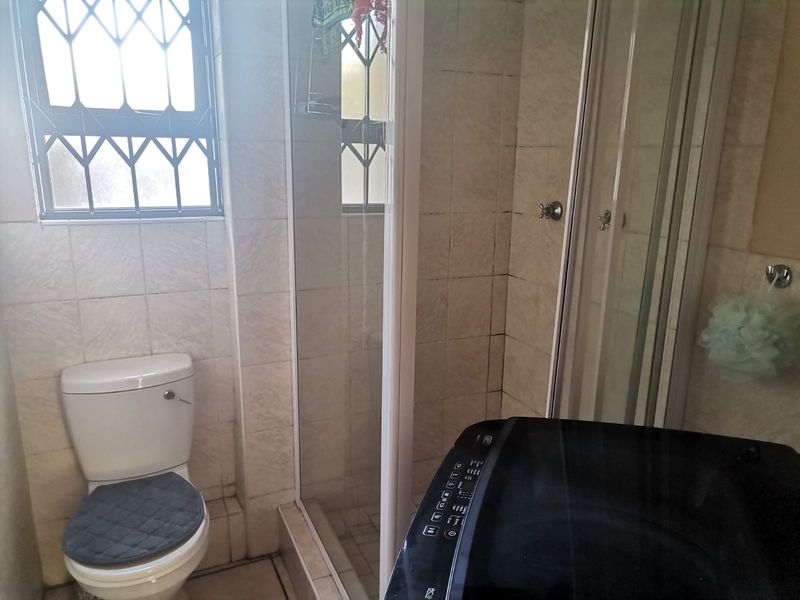 A functional bathroom featuring a shower enclosure, toilet, and tiled wall finishes, with security bars installed on the window.