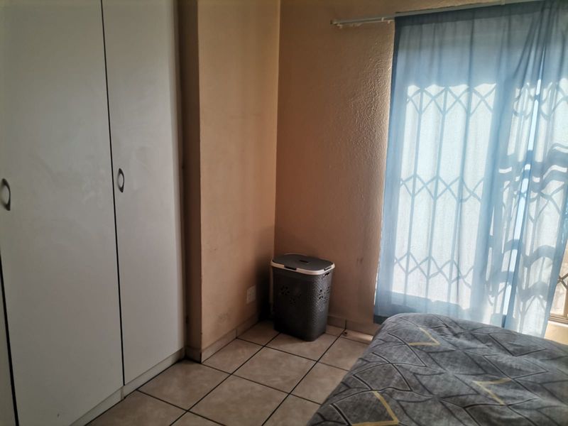 A bedroom featuring tiled flooring, a built-in wardrobe, and a security gate over the window, requiring minor cosmetic updates to the wall finishes.