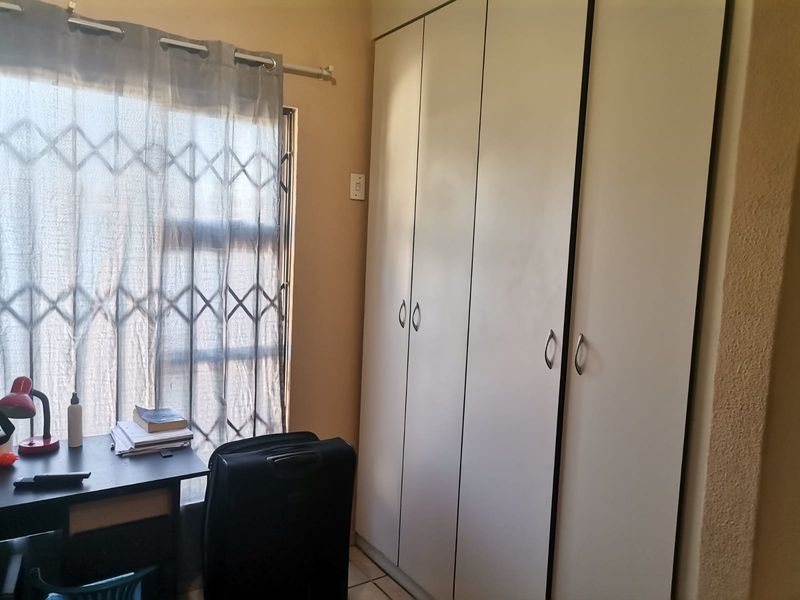A bedroom featuring built-in cupboards, tiled flooring, and a window fitted with a security gate.