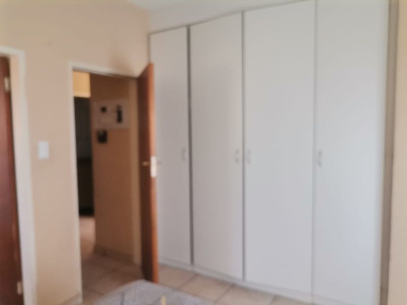 A bedroom featuring built-in cupboards and tiled flooring, providing a functional and neutral space.