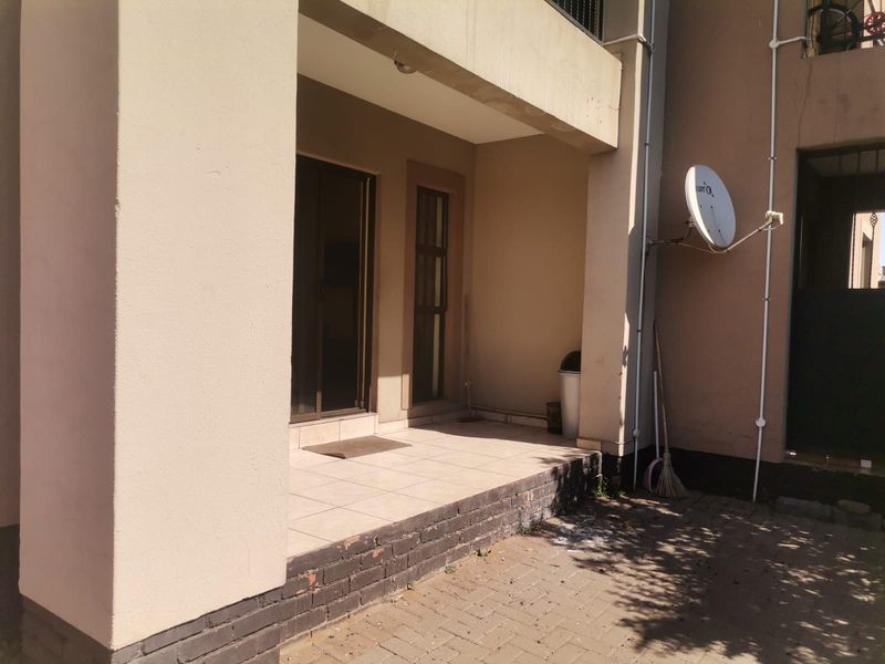 A covered ground-floor patio area featuring tiled flooring, a brick base, and direct access to the apartment interior via a sliding door.