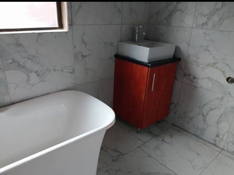 A modern bathroom featuring a freestanding bathtub, a vessel sink vanity, and marble-look wall and floor tiling.