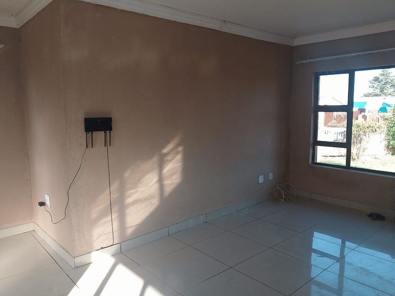 An empty living room featuring tiled flooring, neutral wall finishes, and an aluminium window frame, offering a blank canvas for interior design.