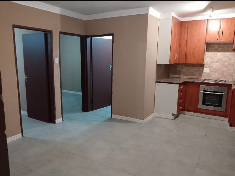 Open plan kitchen featuring wooden cabinetry, built-in oven and hob, tiled flooring, and neutral wall tones, leading to adjacent interior rooms.