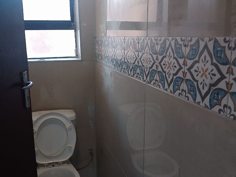 A compact bathroom featuring neutral wall tiles with a decorative accent border, tiled flooring, and a standard toilet.