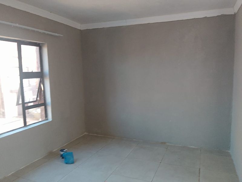 An empty bedroom featuring tiled flooring and an aluminium window frame, currently undergoing renovation with unfinished wall surfaces.