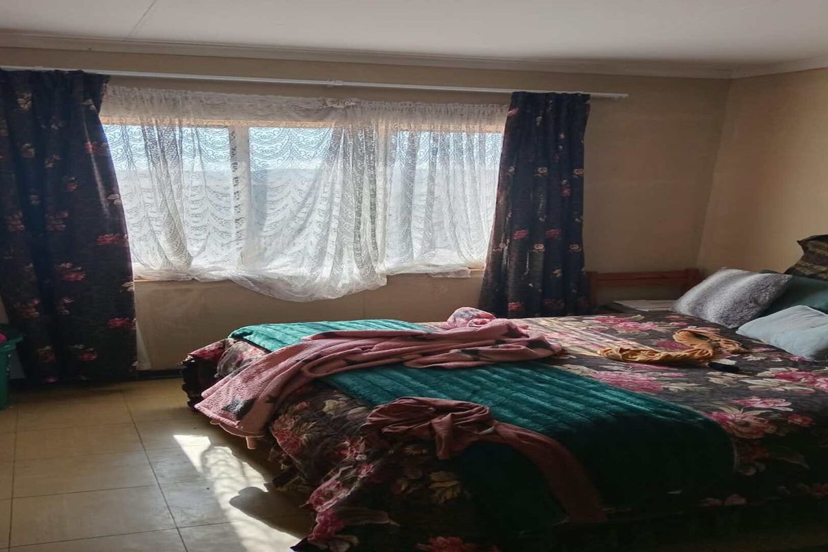 A bedroom featuring tiled flooring and natural light from a window with curtain rails installed.
