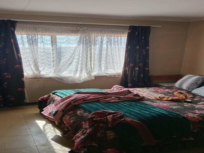 A bedroom featuring tiled flooring and natural light from a window with curtain rails installed.