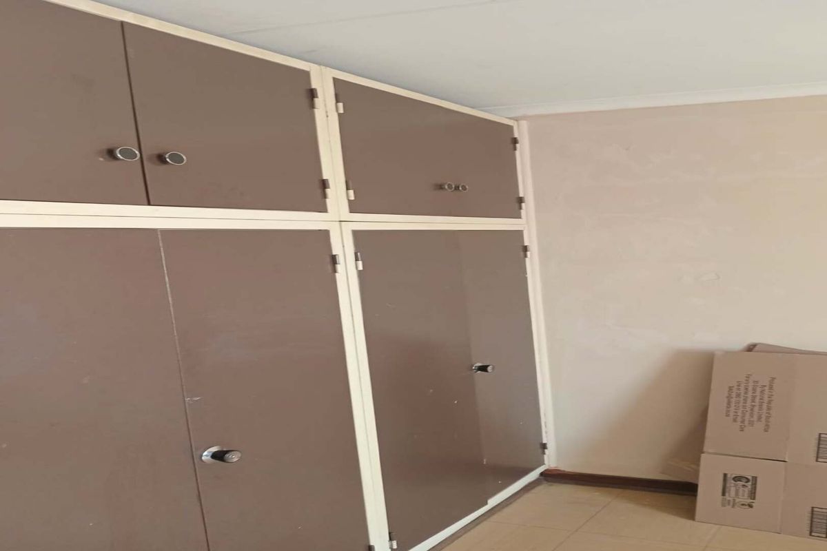 A bedroom interior featuring dated built-in cupboards with brown doors and tiled flooring, currently vacant and in need of cosmetic updates.