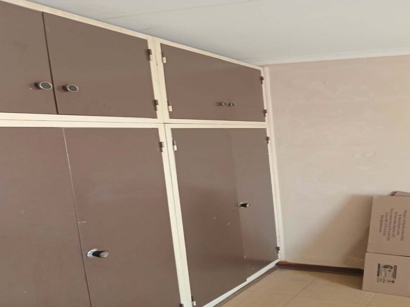A bedroom interior featuring dated built-in cupboards with brown doors and tiled flooring, currently vacant and in need of cosmetic updates.