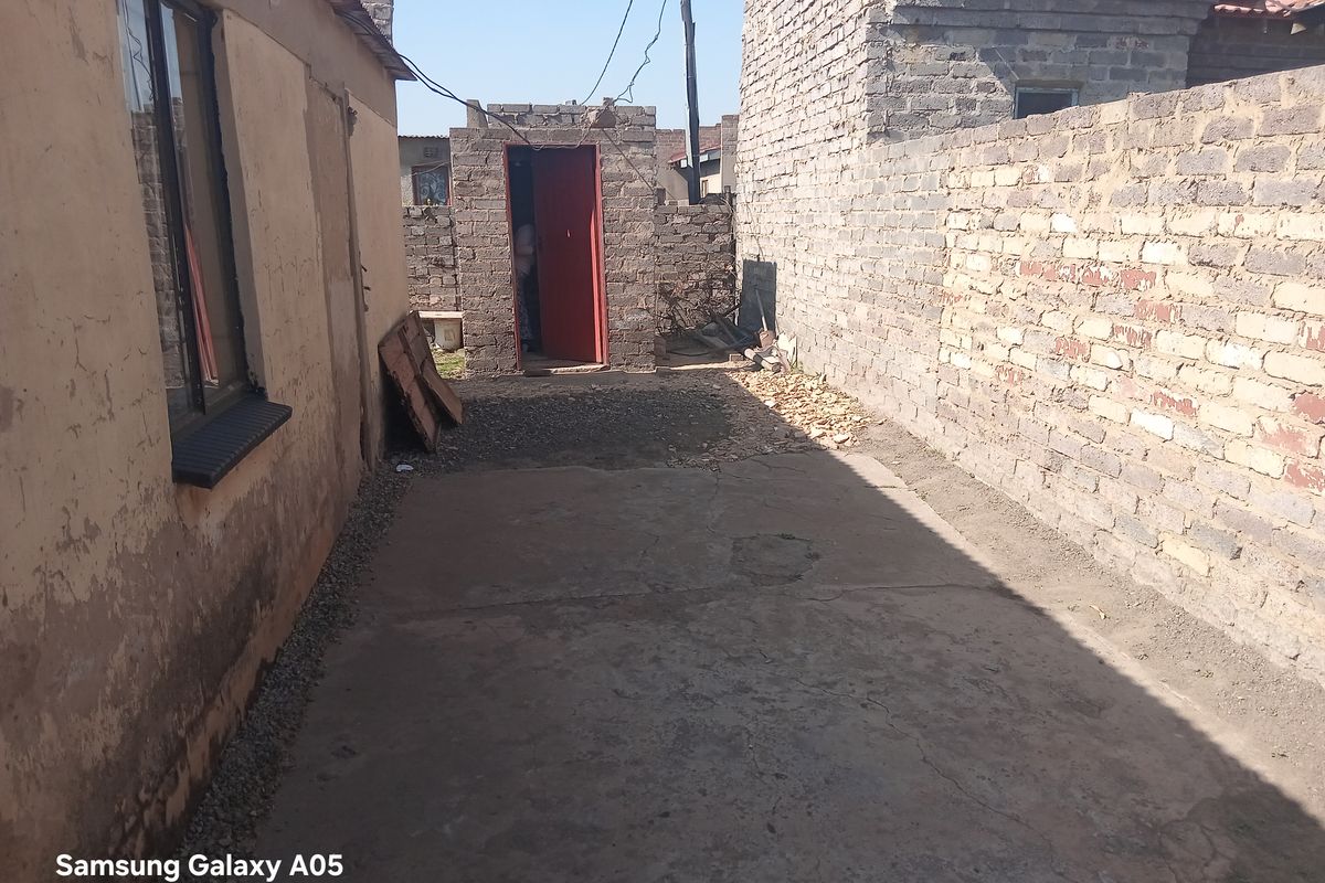 A narrow rear exterior area featuring concrete paving and brick boundary walls, providing access to an external doorway.