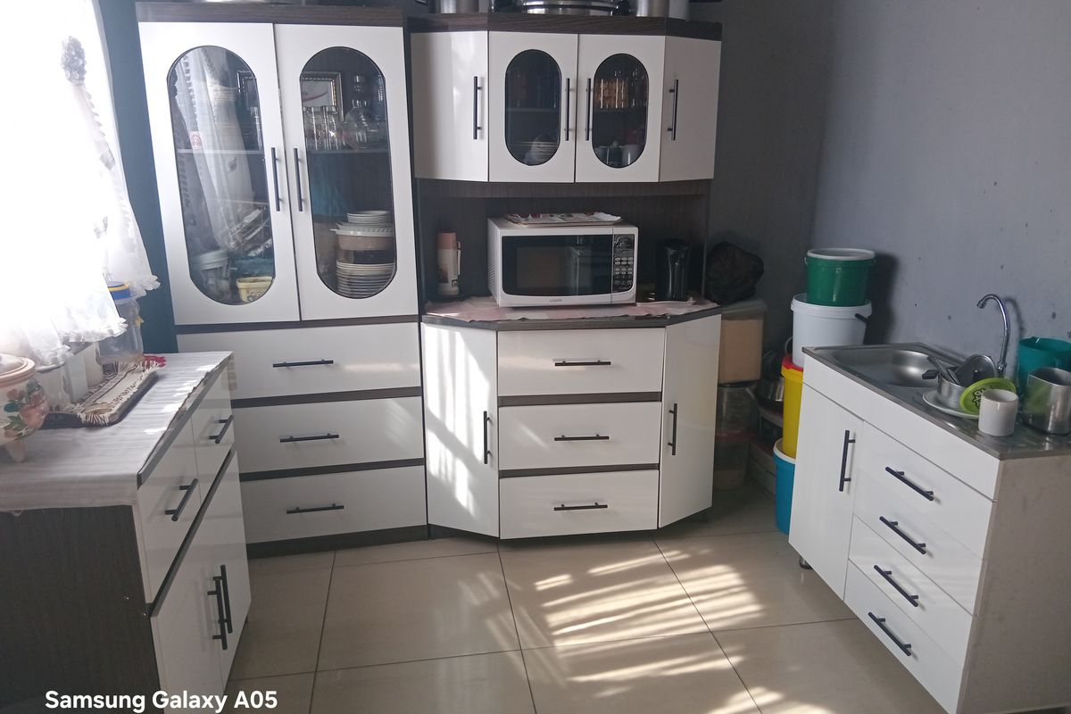 A functional kitchen area featuring white cabinetry, a stainless steel sink, and tiled flooring, providing essential storage and preparation space.