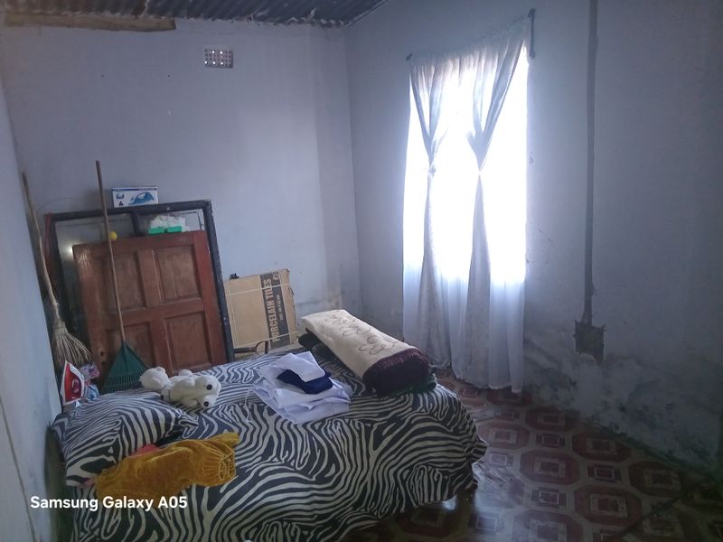 A bedroom featuring tiled flooring and a corrugated iron ceiling, showing signs of wall damp and exposed electrical wiring.