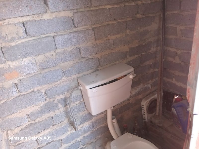A basic bathroom featuring a toilet against unfinished exposed brick walls, requiring significant renovation and finishing to meet standard residential living requirements.