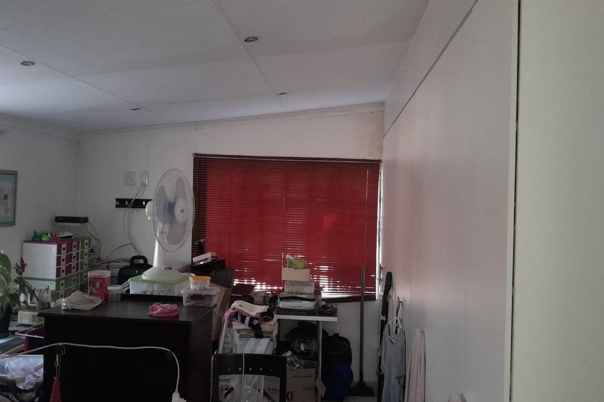 A living room area featuring recessed downlighting and venetian blinds, currently cluttered with personal items and showing signs of wear on the ceiling.