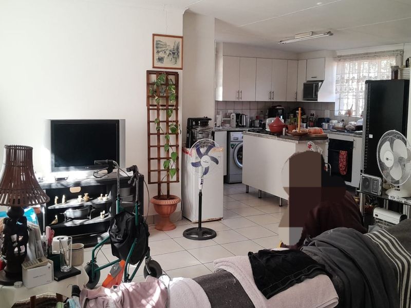 Open-plan living area featuring a functional kitchen with built-in cabinetry, oven, and hob, seamlessly connected to the main living space with tiled flooring throughout.