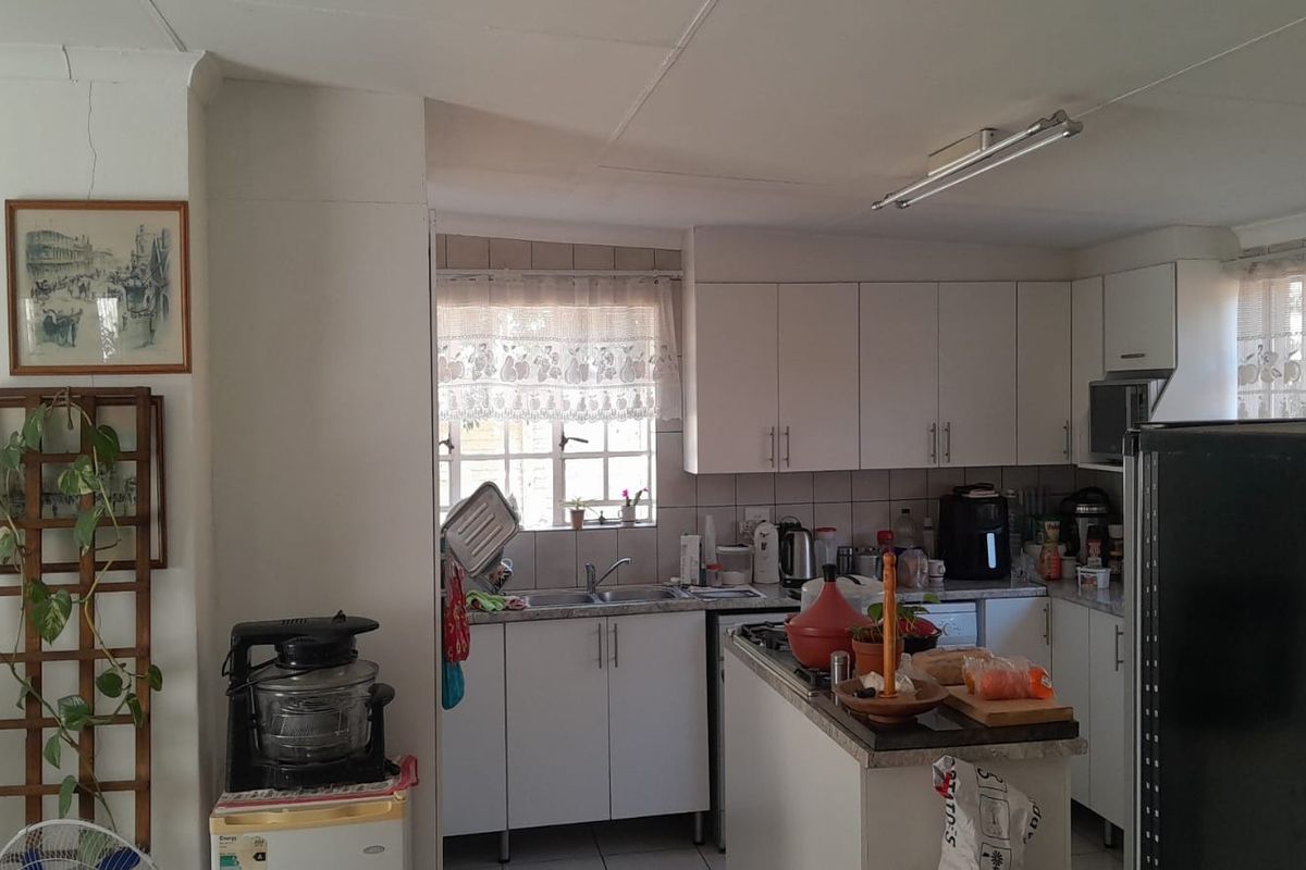 A functional kitchen featuring white cabinetry, laminate countertops, and a tiled backsplash, requiring some cosmetic updates to improve its overall aesthetic appeal.