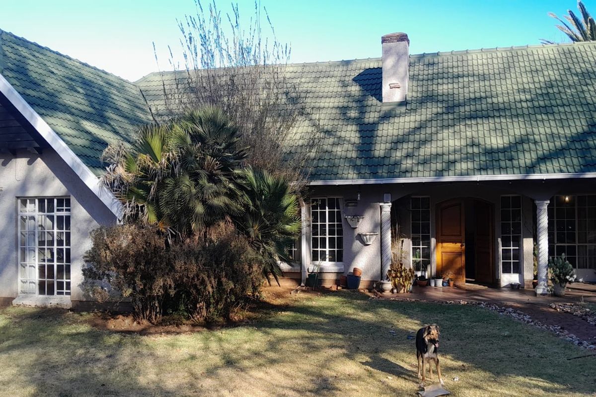 Rear view of a single-story house featuring a tiled roof, chimney, and a covered patio area with decorative columns.