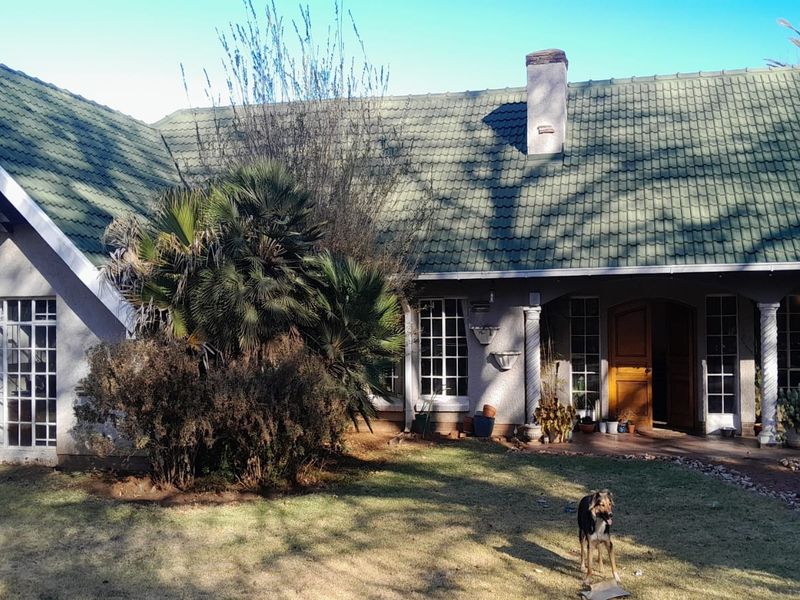 Rear view of a single-story house featuring a tiled roof, chimney, and a covered patio area with decorative columns.