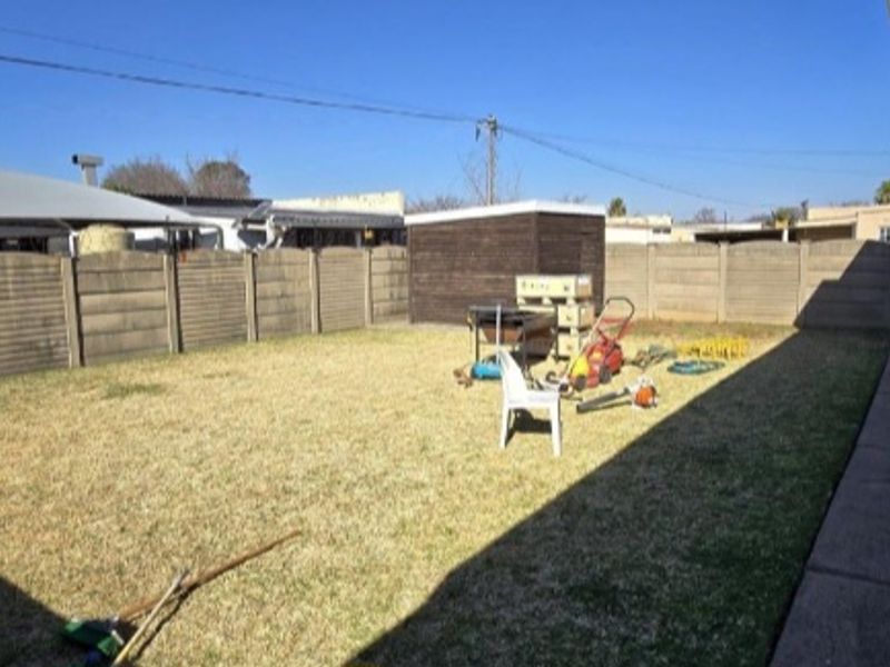 A spacious rear garden featuring a lawn, paved walkway, and a precast concrete boundary wall, offering a blank canvas for outdoor landscaping.