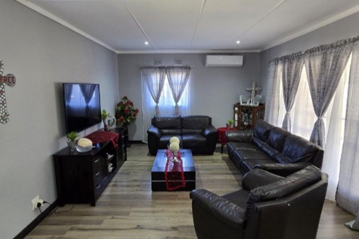 A well-maintained living room featuring modern laminate flooring, recessed downlighting, and a wall-mounted split-system air conditioning unit.