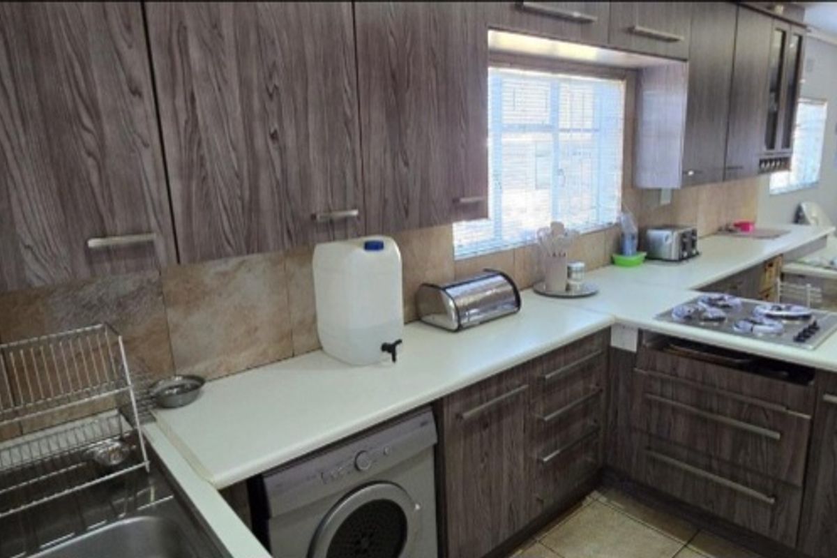 Functional kitchen featuring wood-grain cabinetry, stone-look tile backsplash, built-in gas hob, and integrated laundry space, flowing into an open-plan living area.
