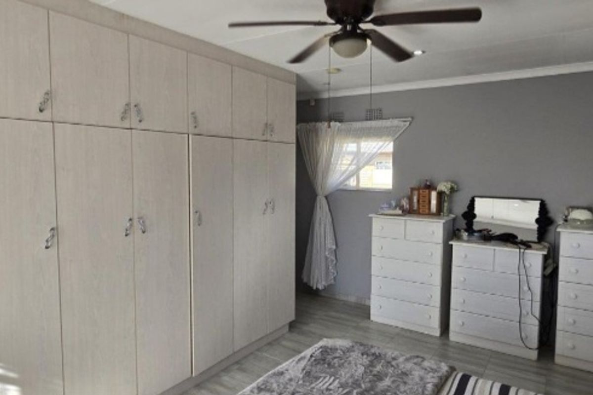 A well-maintained bedroom featuring extensive built-in cupboards, a ceiling fan, and an integrated air conditioning unit.