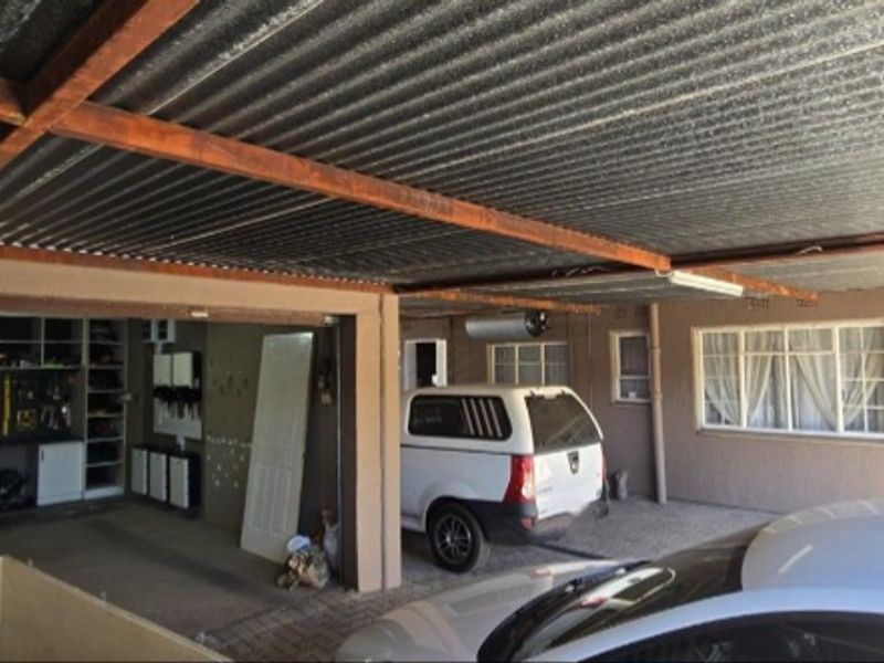 A covered carport and garage area featuring corrugated iron roofing, timber support beams, and built-in storage shelving.