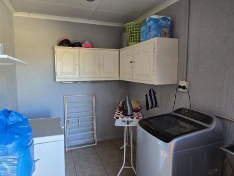 A functional laundry room featuring built-in wall cabinetry, tiled flooring, and a utility sink, providing practical space for household chores.