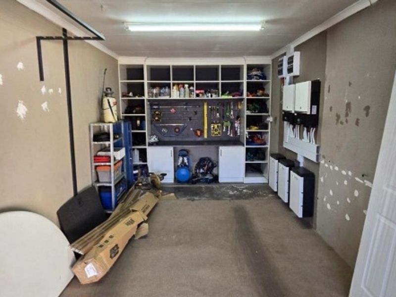 A functional garage space featuring built-in storage shelving and a wall-mounted solar inverter and battery system.