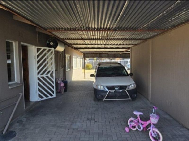 A covered carport area featuring a corrugated metal roof, paved flooring, and a security gate providing access to the main dwelling.