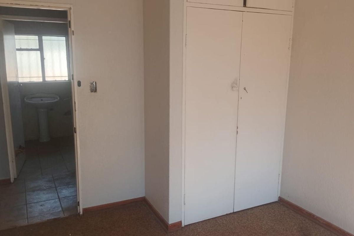 An empty bedroom featuring built-in cupboards and carpet flooring, with an adjacent view into a bathroom area.
