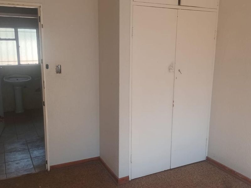 An empty bedroom featuring built-in cupboards and carpet flooring, with an adjacent view into a bathroom area.