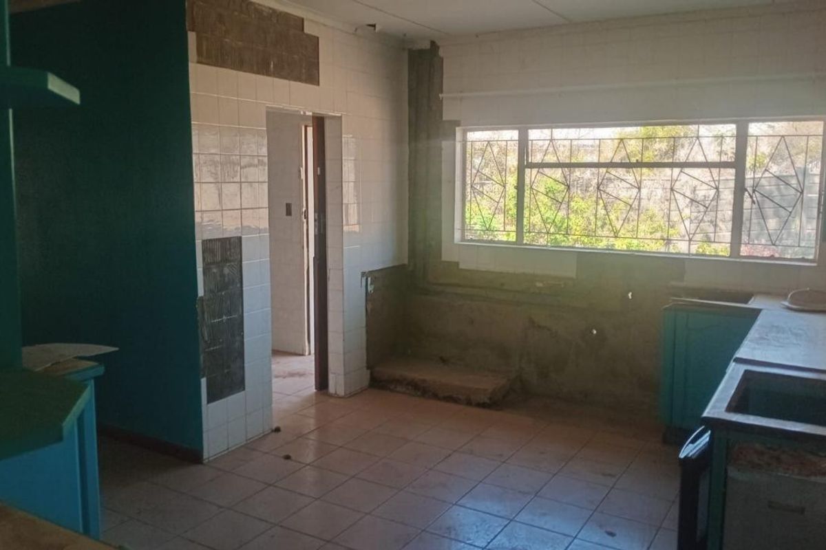 A kitchen in need of renovation, featuring tiled flooring, built-in cabinetry, and significant wall surface damage requiring repair and modernization.