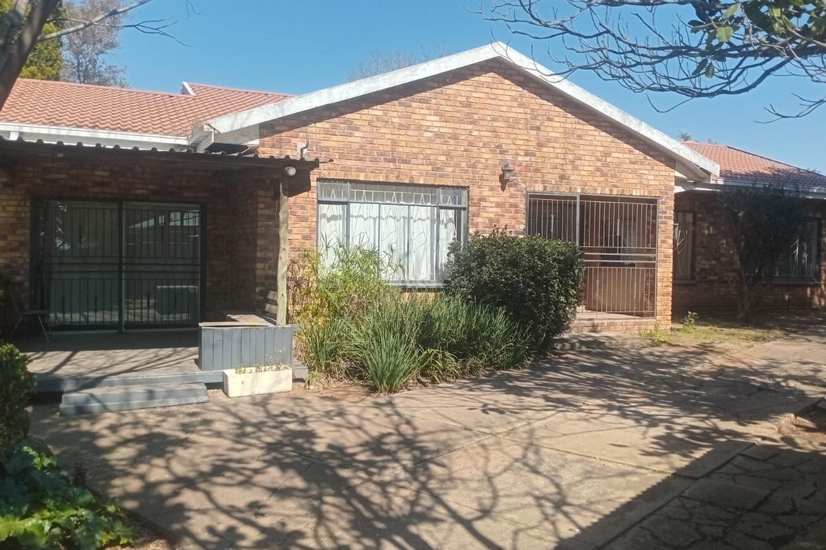 Rear view of a face brick house featuring a paved patio area, sliding glass doors with security gates, and a tiled roof.