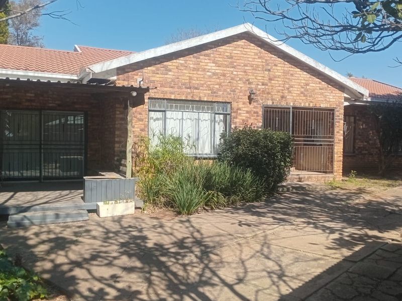 Rear view of a face brick house featuring a paved patio area, sliding glass doors with security gates, and a tiled roof.