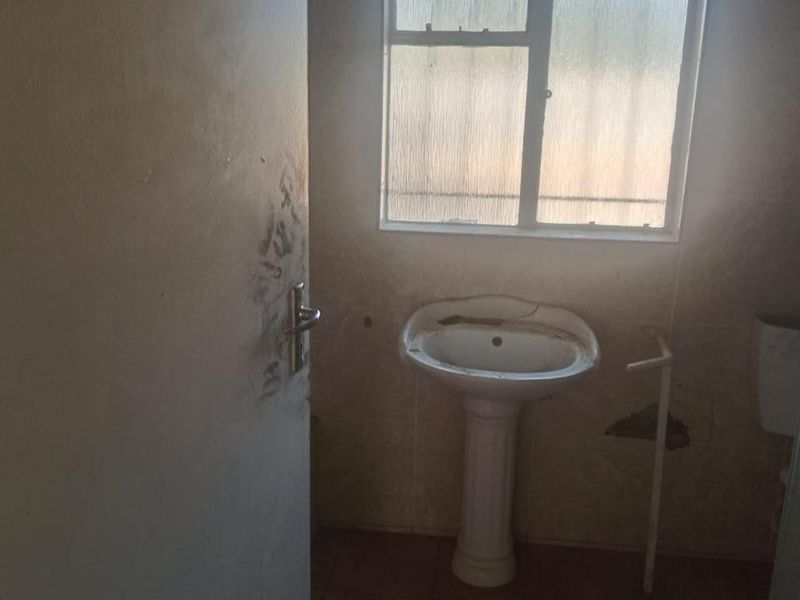 A small bathroom featuring a pedestal basin and tiled finishes, currently in need of significant maintenance and cosmetic renovation.