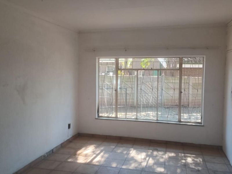 An empty bedroom featuring tiled flooring, built-in cupboards, and large windows with security bars, requiring cosmetic updates to refresh the space.