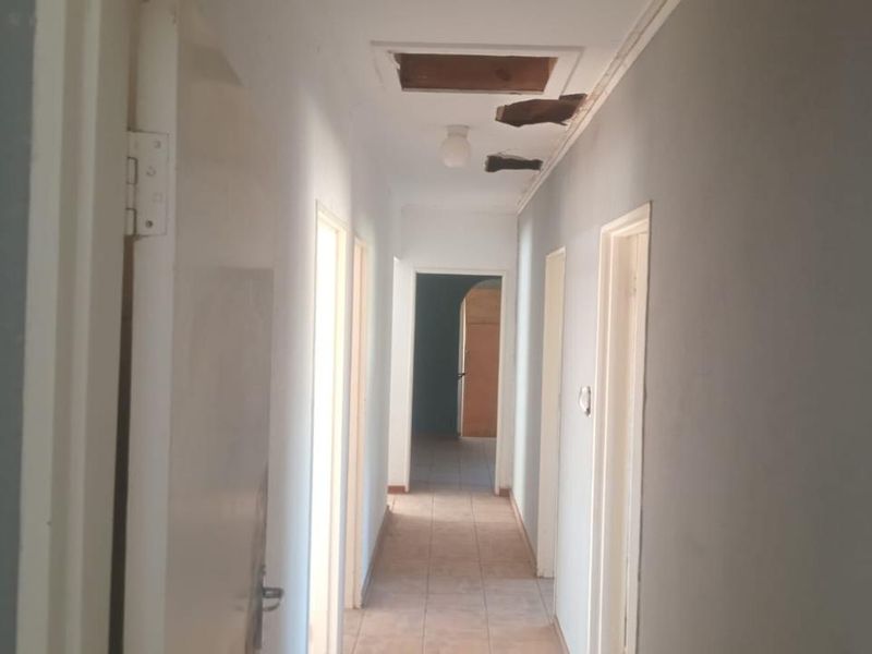 A vacant hallway featuring tiled flooring and visible damage to the ceiling plaster near the access hatch.